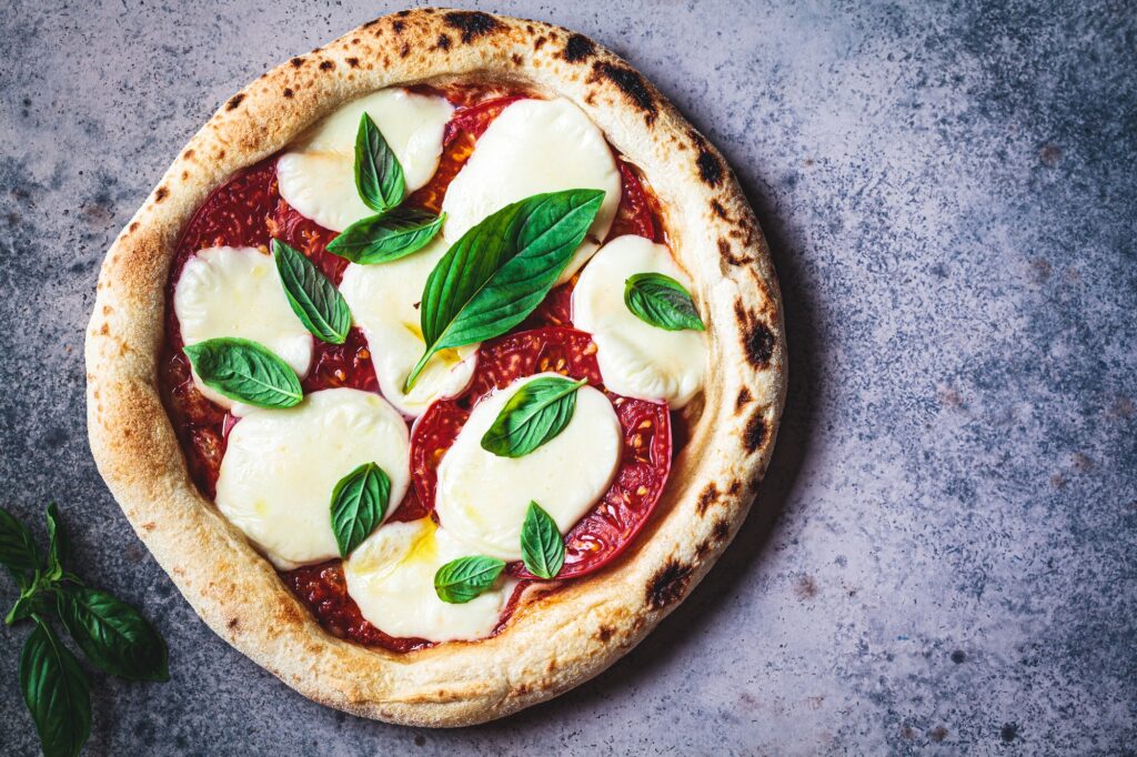 Classic neapolitan margherita pizza with tomatoes, mozzarella and basil on dark background.