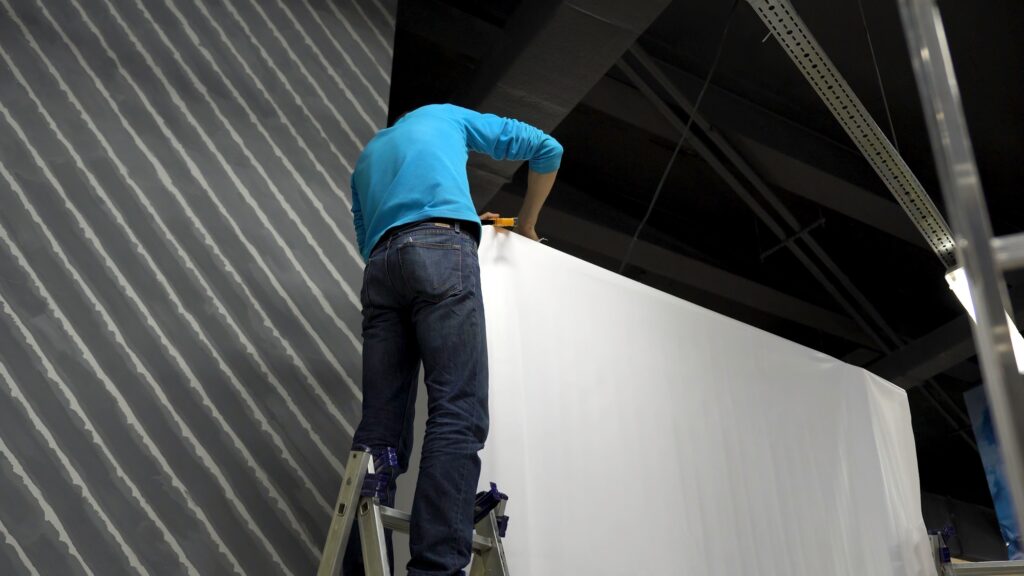 Worker builds a concert stage. Worker in blue shirt standing on stepladder, installing big stand