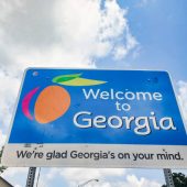 This is a photograph taken of the Welcome to Georgia sign marking the state line at the border on a sunny day with clouds during the summer of 2020